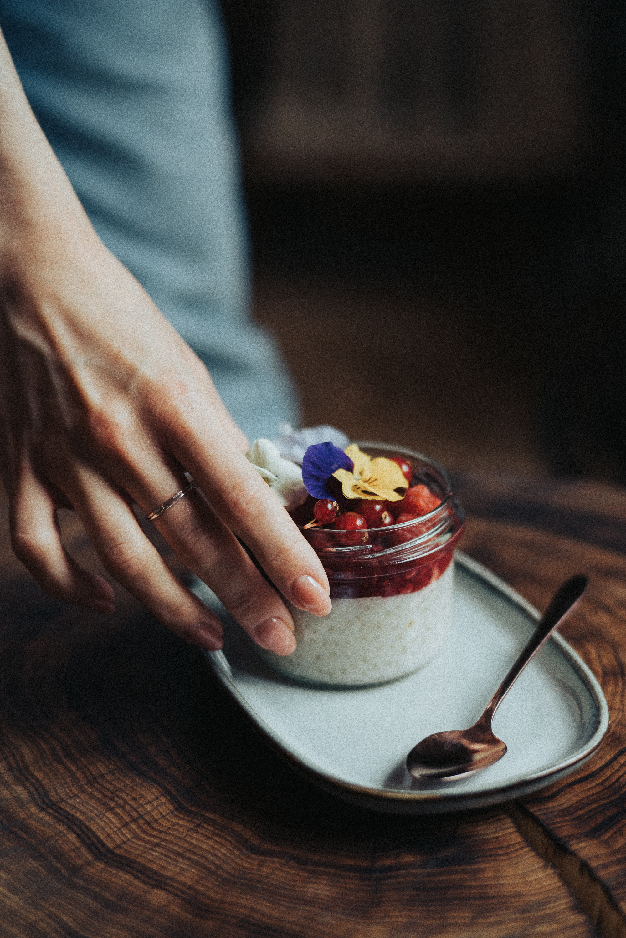 Stack of pancakes topped with berries and syrup on a white plate, set on a rustic wooden table with a blurred kitchen background, evoking a cozy and inviting mood
